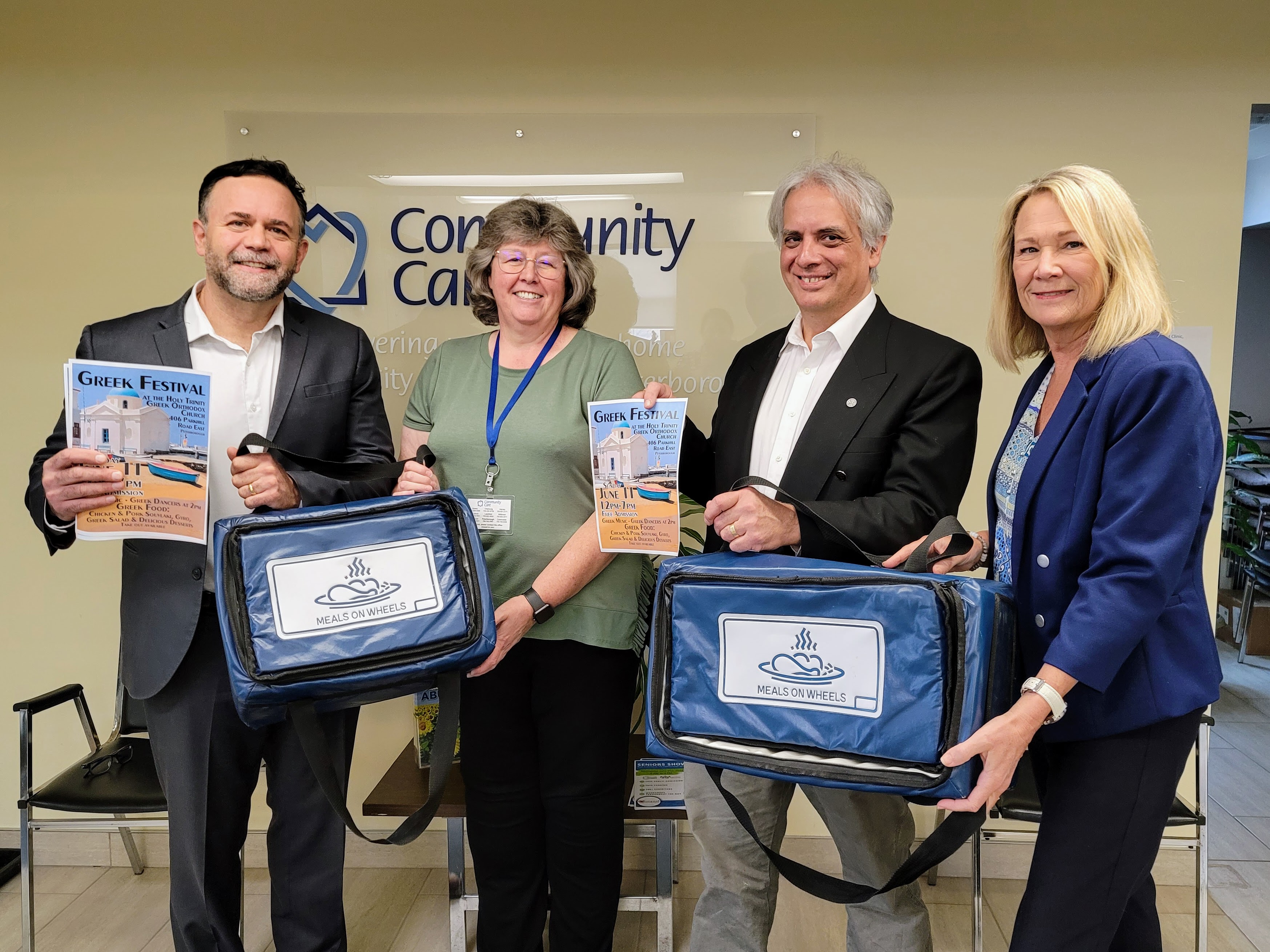 Picture taken at Community Care Peterborough office, left to right: Councillor Don Vassiliadis, Iris Crowder – Client Service Coordinator and Meals to Go fundraiser coordinator for CCP, Dean Pappas and Catherine Pink – Director, Support Services at CCP. holding poster of Greek Festival and Meals on Wheels delivery bags